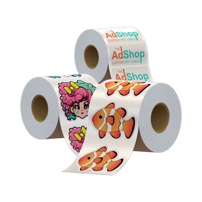 The image shows three rolls of die-cut stickers on a white background. The first roll features a single clownfish seen three times on the roll, the second roll has a sticker of a young girl with wildly colourful hair and a yellow bow, and the third roll features a rectangular white label with The Ad Shop logo.
