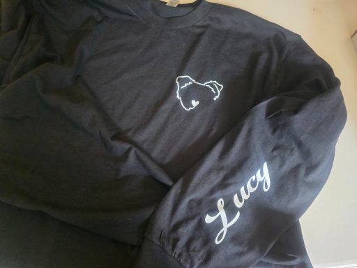 Black shirt with a drawing of a dog and the name "Lucy" pressed on one sleeve.