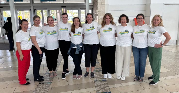 A group of ten people wearing matching white t-shirts standing together, smiling.