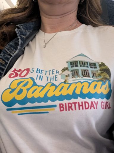 Person wearing a "Birthday Girl" shirt with a Bahamas theme, featuring colorful text and a house illustration.