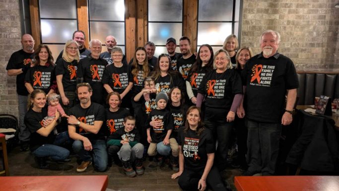 Group photo of people wearing matching black shirts, smiling and posing together. MS Support Shirts.