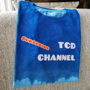 Blue t-shirt with "Subscribe TCD Channel" printed in white and orange text.