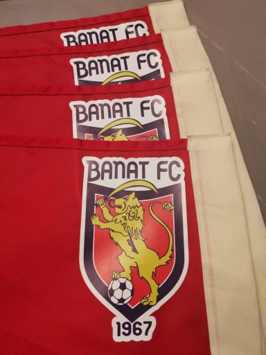 Flags with Banat FC, featuring a lion emblem and soccer ball, with red and beige colors.